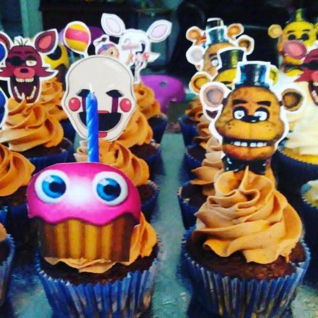 Cupcakes with Five Nights at Freddy&rsquo;s character toppers and a lit birthday candle