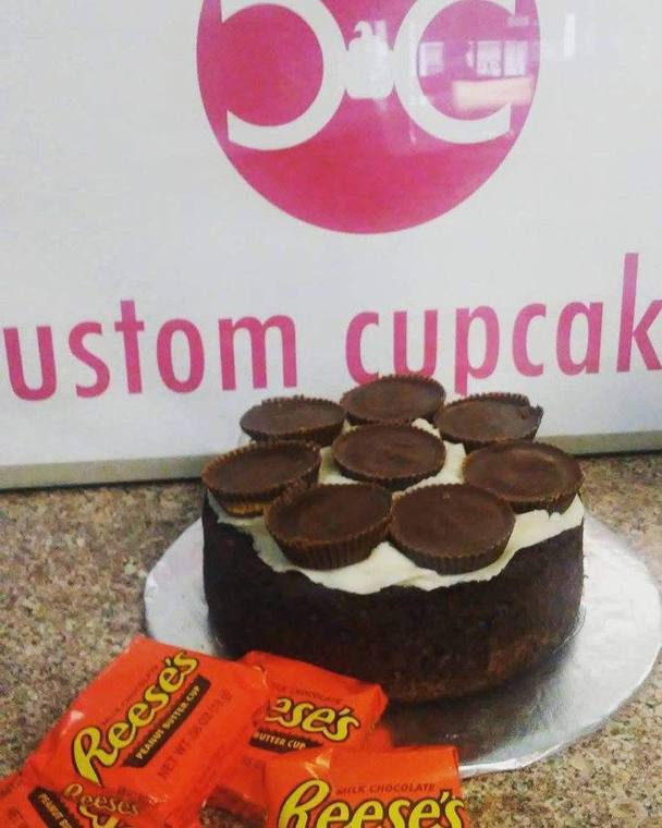 A chocolate cake ringed with Reese&rsquo;s peanut butter cups in front of the Custom Cupcakes banner