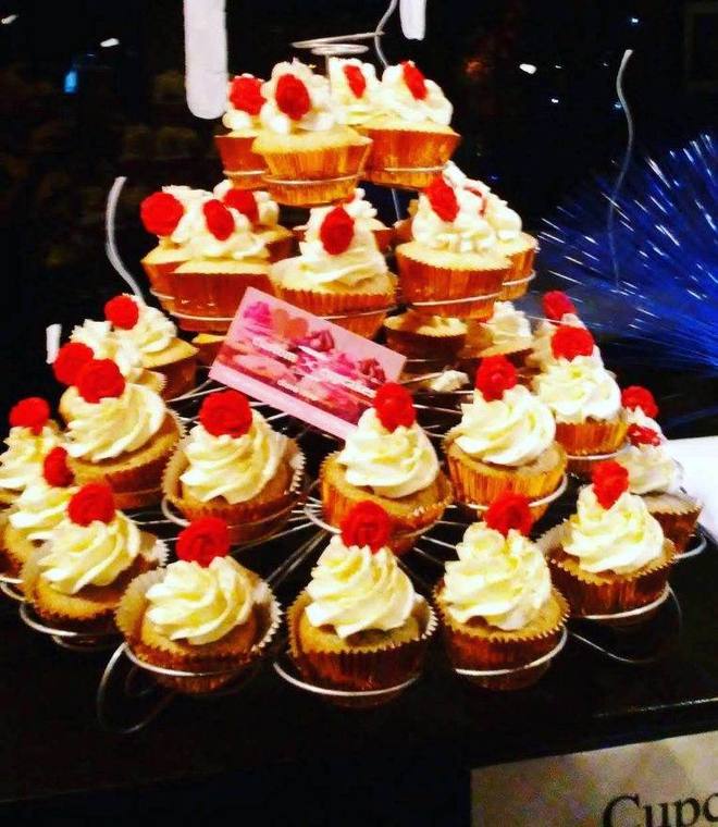 A tiered stand of white-frosted cupcakes each topped with a red sugar rose
